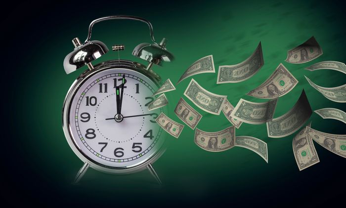 Alarm clock with flying dollar bills symbolizing time is money.