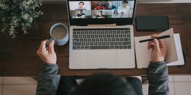Person holding a cup and pen during a virtual meeting on a laptop.