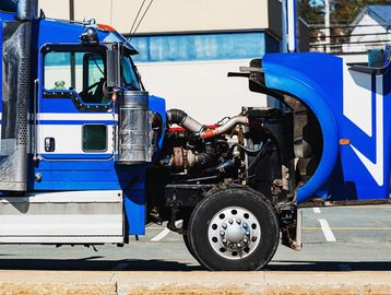 Blue semi-truck with open hood showing engine components in a parking lot.