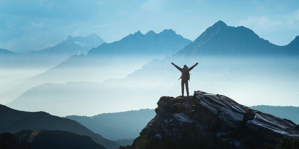 Hiker celebrates on a mountain peak with misty mountains in the background.