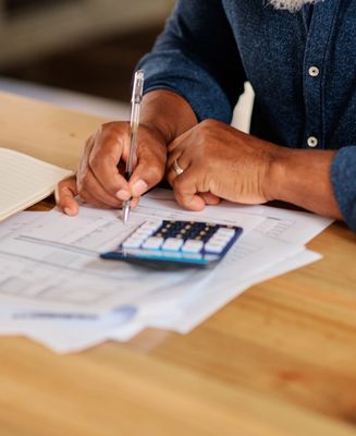 Person calculating finances with pen, calculator, and documents.