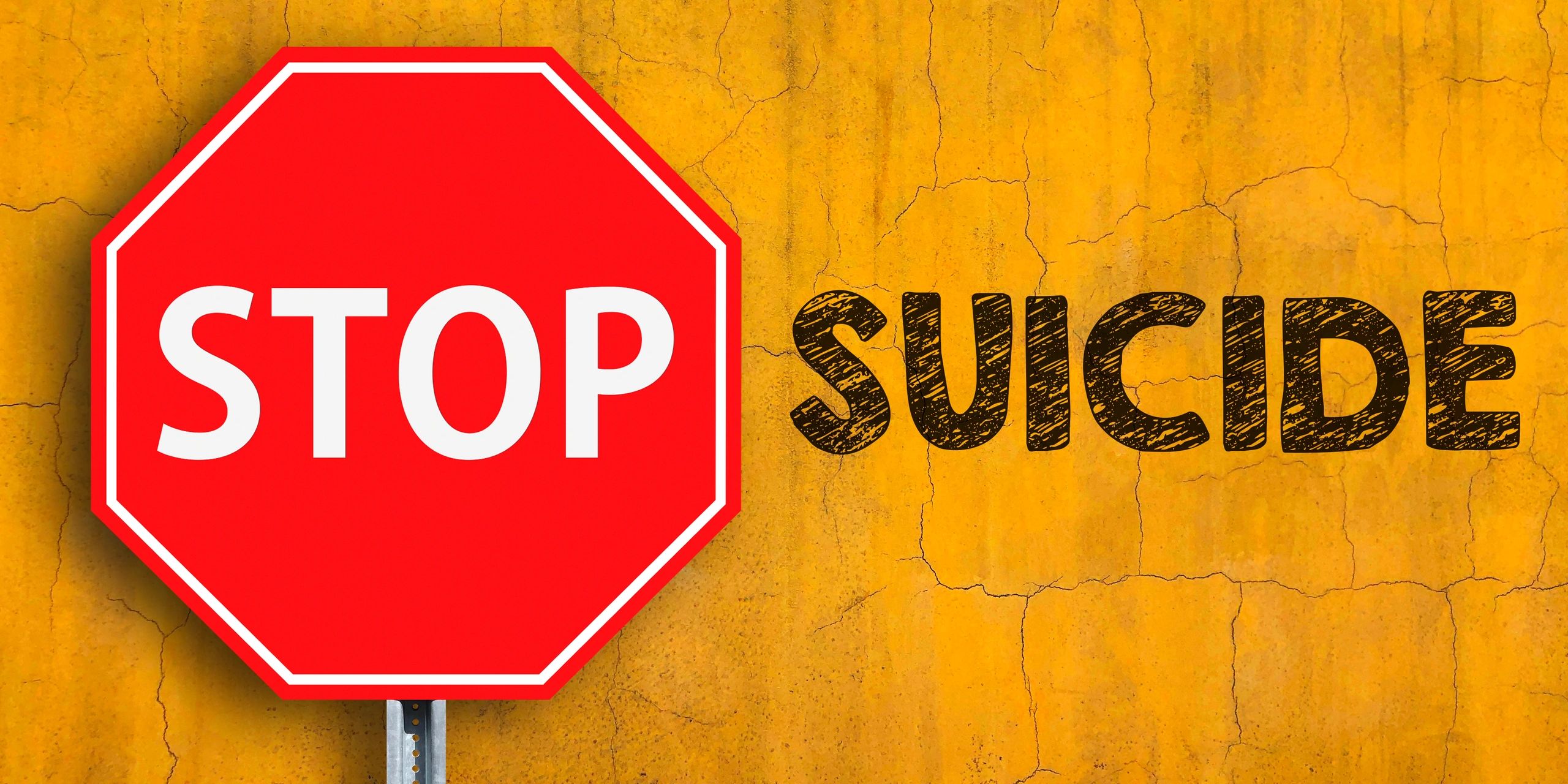 Red stop sign and word 'SUICIDE' on cracked yellow wall.