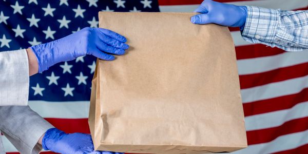 Two people exchanging a paper bag with an American flag backdrop.