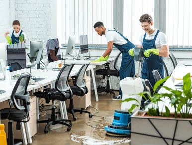 Three janitors cleaning a modern office space with floor cleaner and wipes.