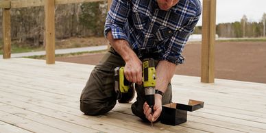 Man using a power drill to fix wooden deck boards outdoors.