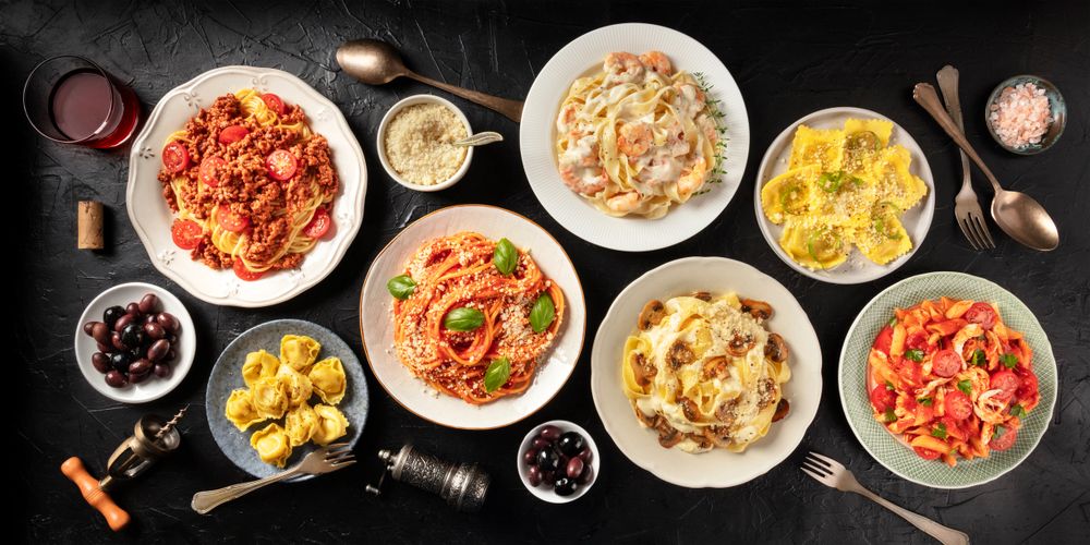 Various plated pasta dishes with different sauces and garnishes on a dark surface.