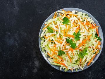 Fresh cabbage and carrot salad garnished with parsley on a gray plate.