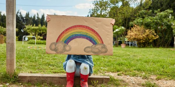 Child holding a drawing of a rainbow outdoors.
