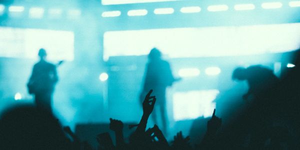 Blurred silhouettes of a band performing on stage with an energetic crowd.