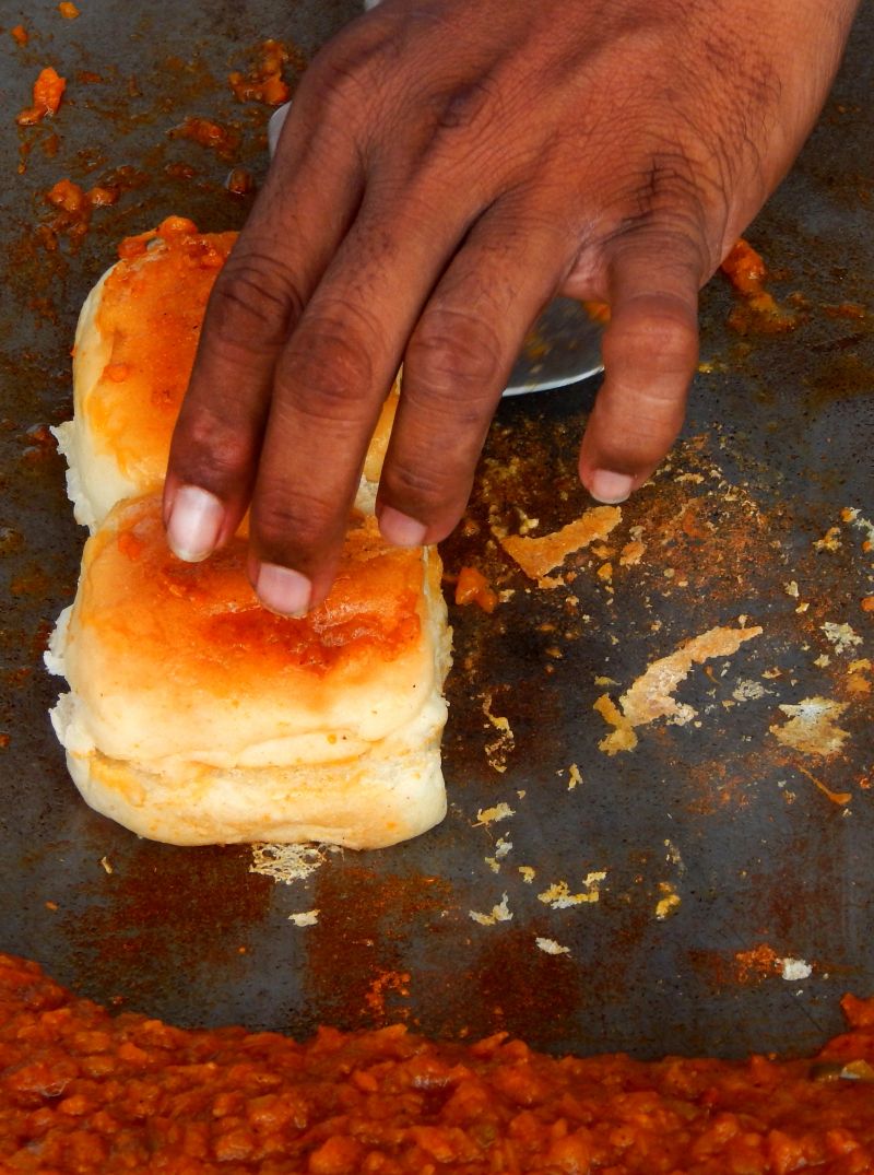 Indian street food vendor making vada pav,filling bread with masala