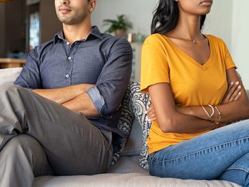 Man and woman sitting back-to-back with arms crossed, showing disagreement.