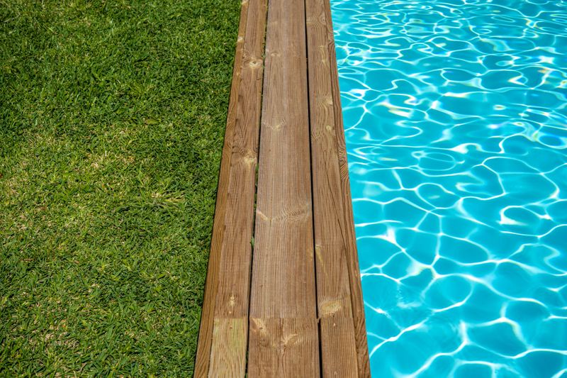 Clear water swimming pool with wooden deck and green grass around