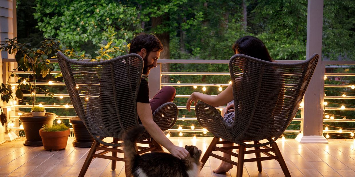 Couple relaxing on a porch with string lights and a cat.