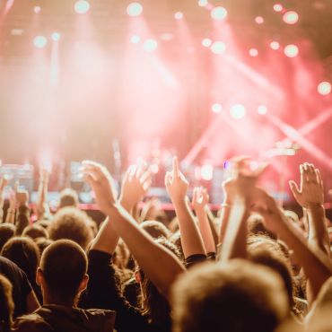 Crowd enjoying a lively concert with raised hands and bright stage lights.