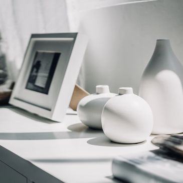 Minimalist white vases and framed photo on a sunlit table.