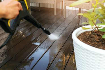Person pressure washing a wooden deck on a sunny day.