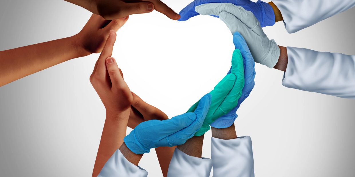 Hands forming a heart symbol with medical gloves and bare hands.
