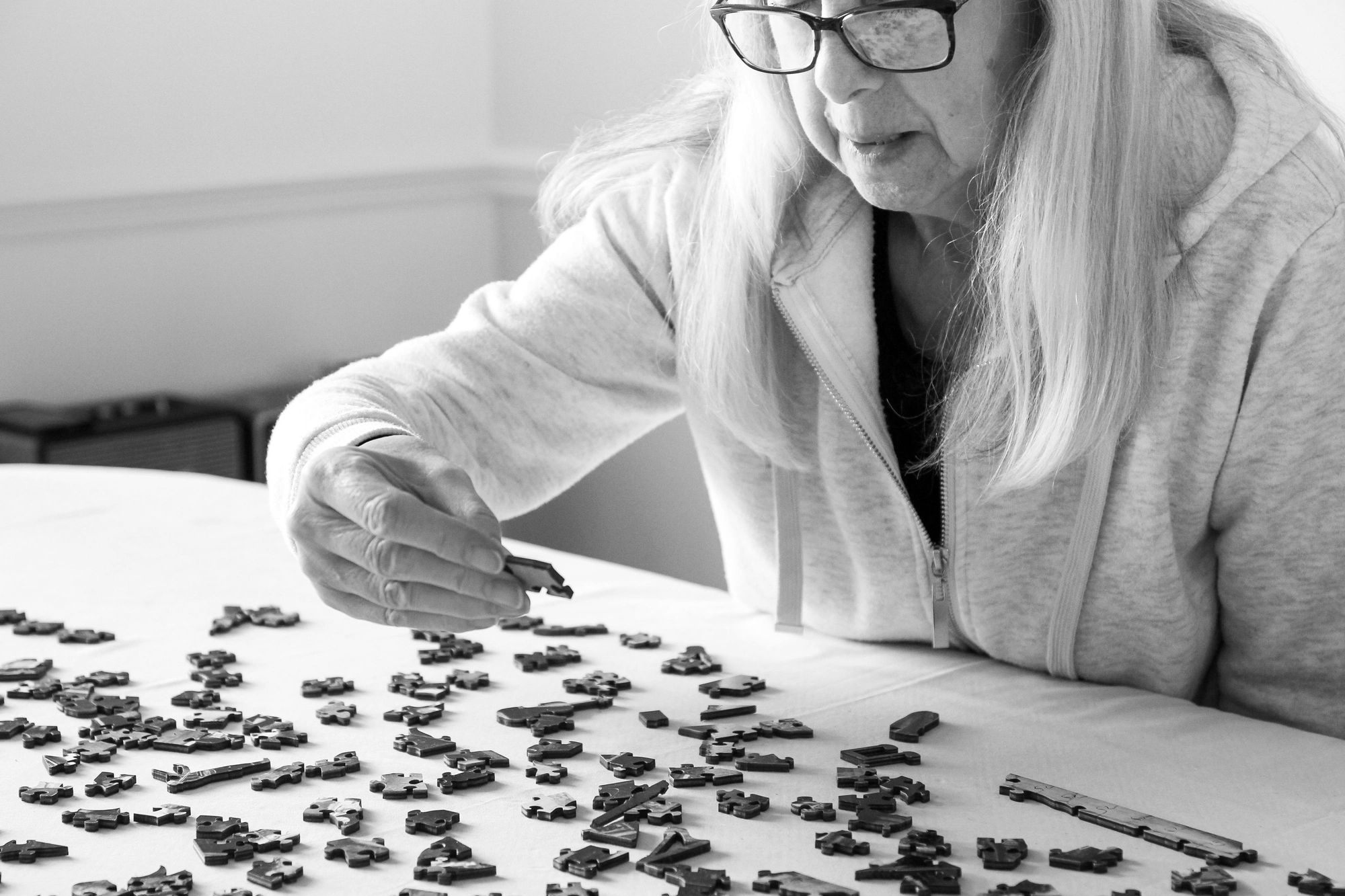 Elderly woman assembling a puzzle on a table, focused and engaged.