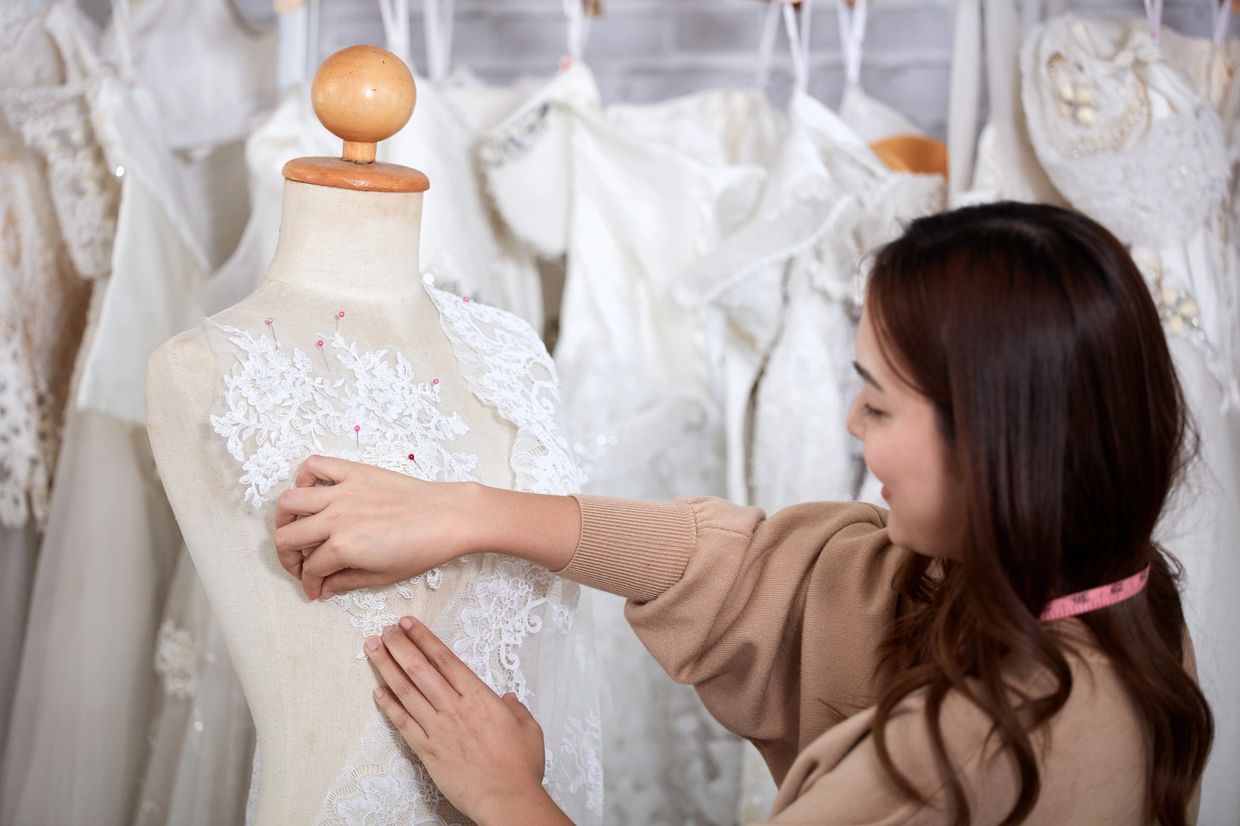 A woman fitting lace fabric on a dress mannequin in a bridal shop.
