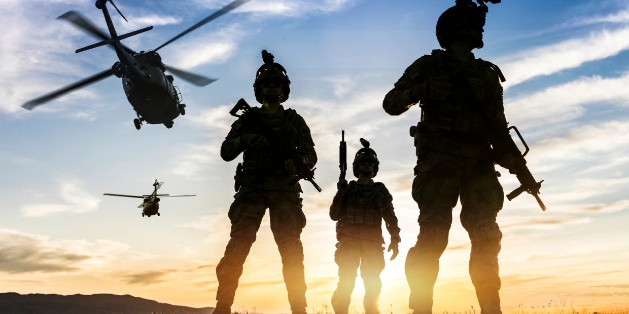 Silhouetted soldiers with helicopters at sunset.