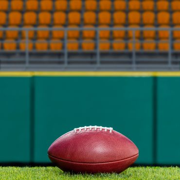 Football on a field with stadium seats in the background.