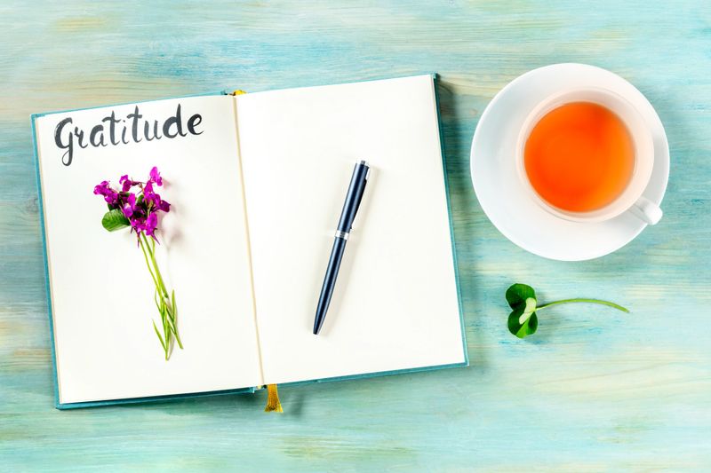 Gratitude journal with a pen, a flower, and a cup of tea, shot from the top, with the handwritten word