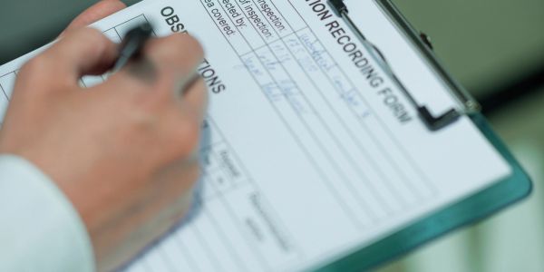 Person filling out an inspection recording form on a clipboard.