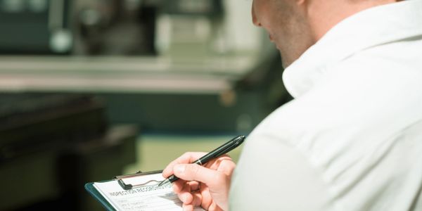 Man in white shirt writing on a clipboard with a pen.