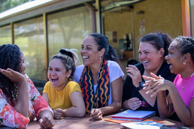Young aboriginal female students sitting with their tutor outdoors in the sun in Australia.