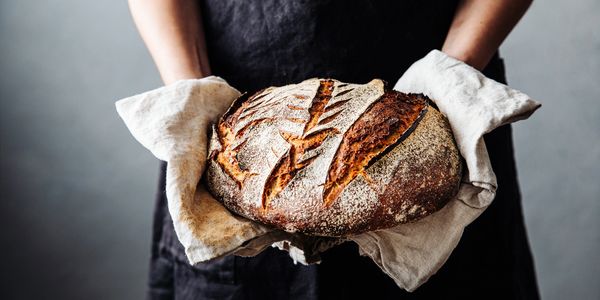 Person holding a freshly baked artisan loaf of bread with oven mitts.