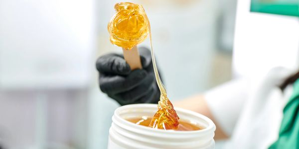 Person holding a wooden stick with golden wax for hair removal.