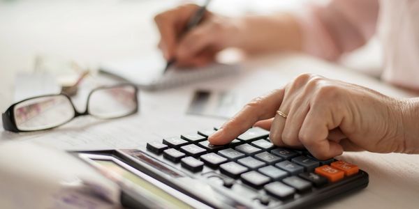 Person using a calculator and writing notes, with glasses nearby.