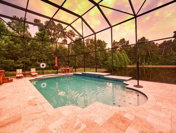 Enclosed swimming pool with seating and lush greenery outside.