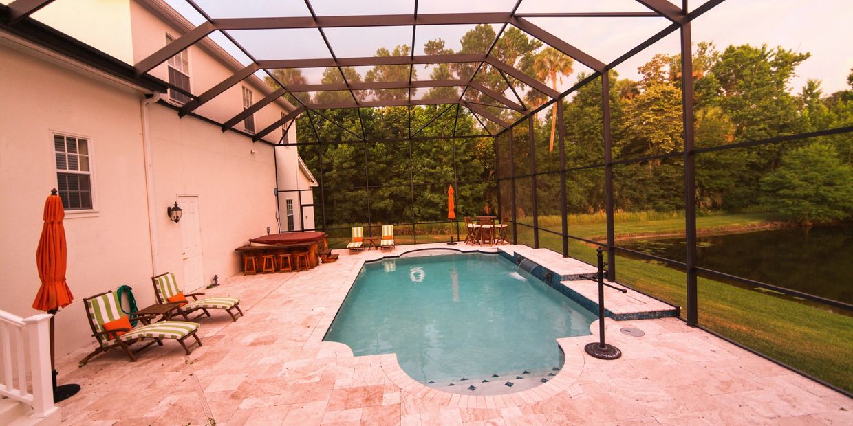 A screened-in pool area with lounge chairs and green trees outside.