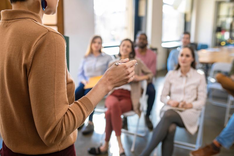 Back view of a woman lecturer giving presentation on business training to a group of businesspeople.