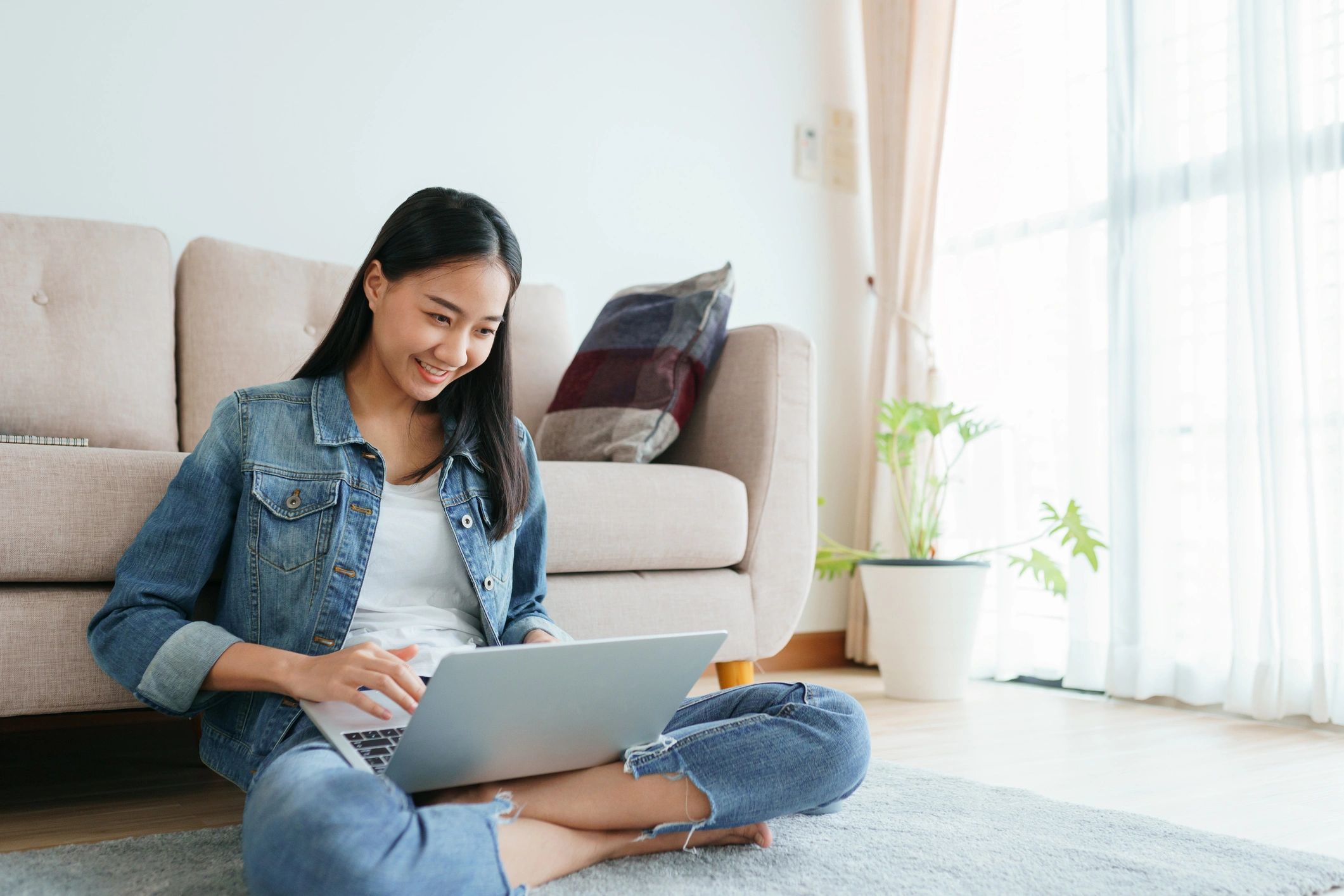Young woman sitting on the floor using a laptop with a smile.