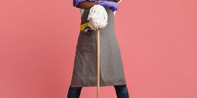 Man in apron and gloves leaning on mop against pink background.