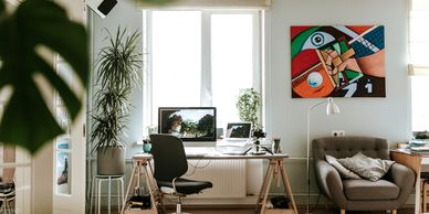 Modern home office with computer, plants, and colorful abstract wall art.