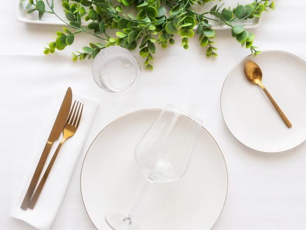 Elegant table setting with gold utensils and greenery centerpiece.