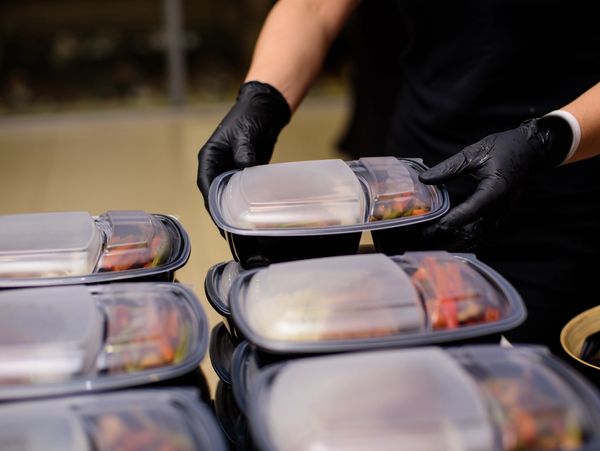 Hands in black gloves holding stacked food containers.