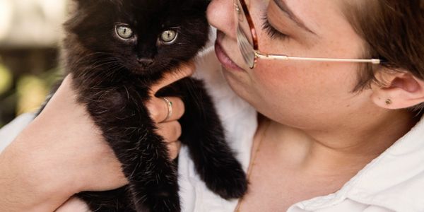 Person lovingly holding a fluffy black kitten.