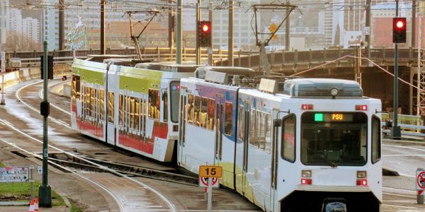 A light rail train on tracks in an urban setting with city buildings in the background.
