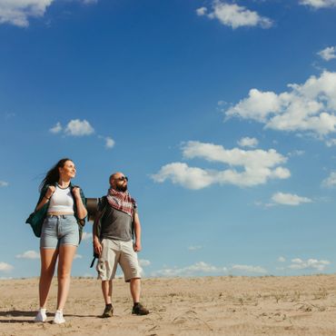 A man and woman hiking in a desert under a bright blue sky.