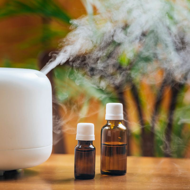 Natural essential oil bottles and aroma therapy diffuser on a wooden table. Scented steamy atmosphere in the background for comfortable living