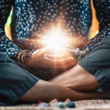 Person meditating with glowing light between hands, wearing starry shirt and bracelets.