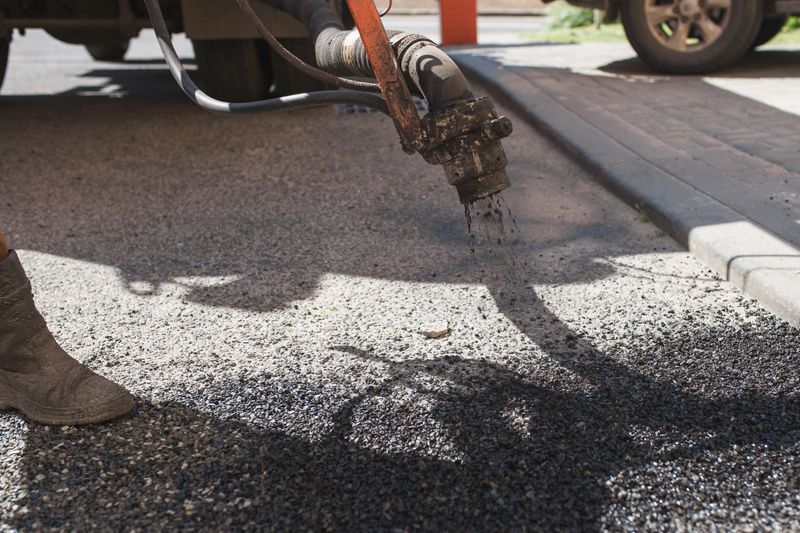 Road works using hot bitumen emulsion and crushed stone during asphalt patching