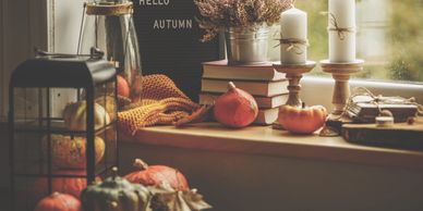 Cozy autumn display with pumpkins, candles, and a 'Hello Autumn' sign on a windowsill.