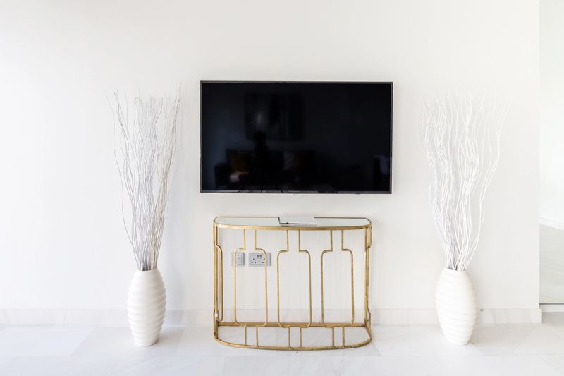 Big TV Screen on a White Wall Inside a Luxurious Apartment with Vases on the side
