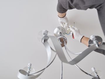 Person installing a chandelier on the ceiling.