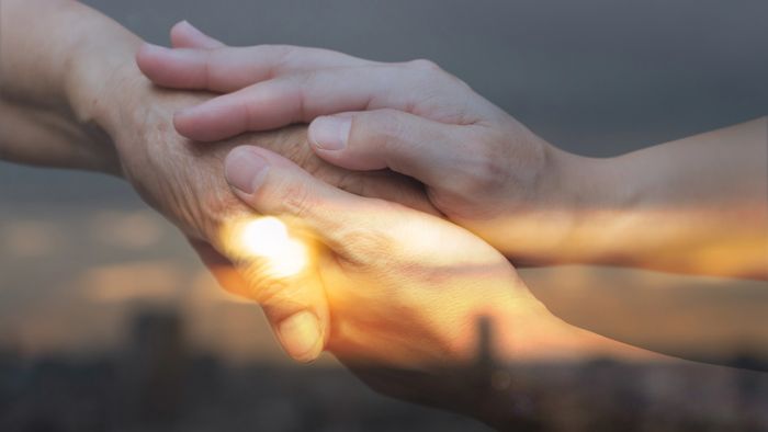 Two hands gently holding each other against a sunset backdrop.